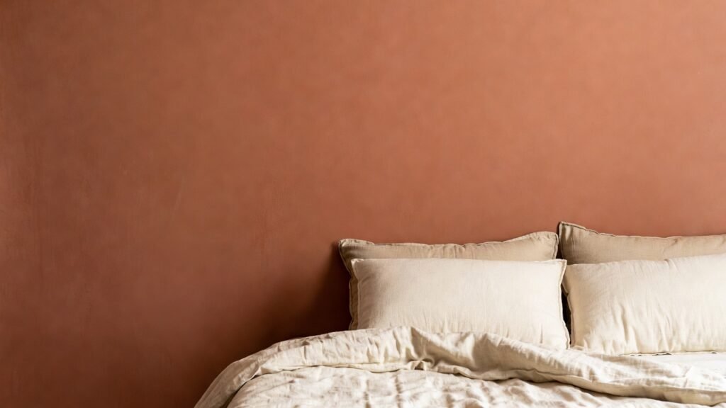 A bedroom wall painted in a soft terracotta hue with cream-colored bedding, demonstrating a balanced earth-element color palette.